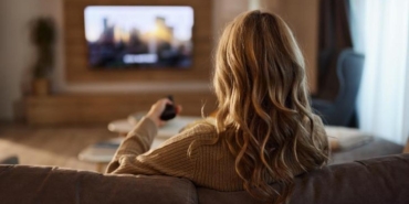 Back view of relaxed woman watching TV at home.