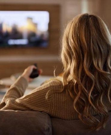 Back view of relaxed woman watching TV at home.